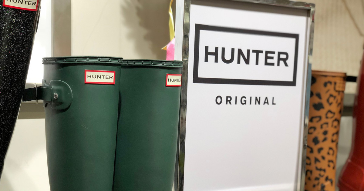 pair of matte green hunter brand rain boots next to store display sign for hunter brand
