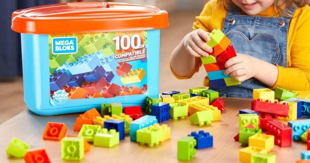 little girl playing with chunky style blocks at table with pieces spread out in front of storage bin