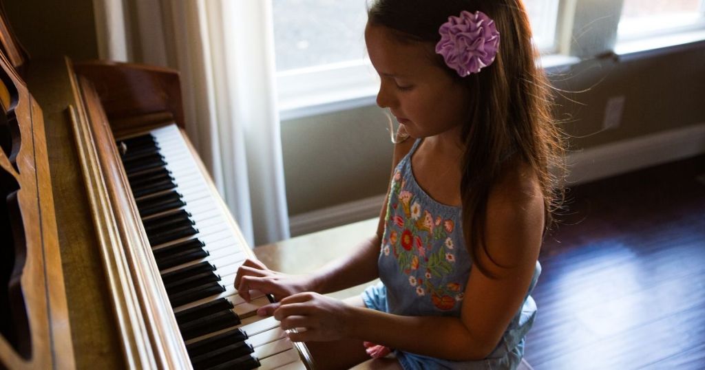 Little girl sitting on piano bench and playing piano