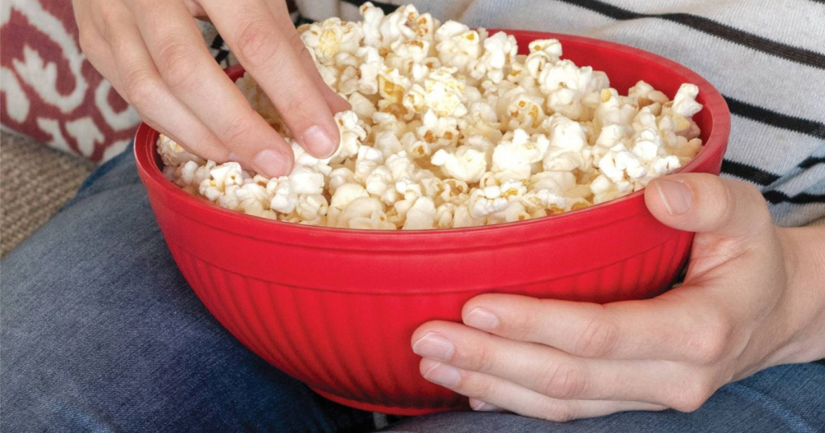 hands picking popcorn out of red bowl on lap