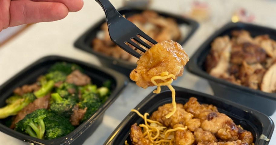 Orange chicken on fork hovering over Panda Express bowls