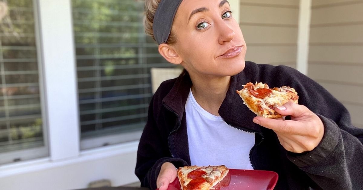 Woman holding a plate with Red Baron pizza and taking a bite of a slice