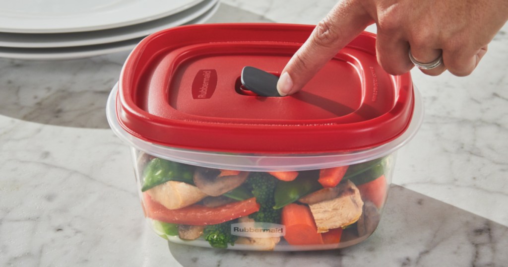 finger pressing on food container red vented lid on counter next to stack of three white plates