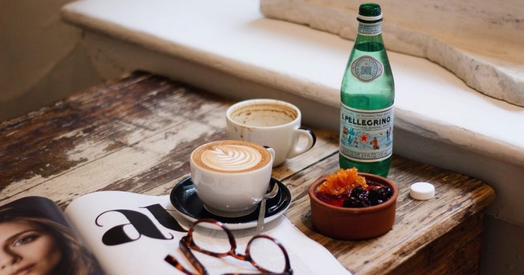 table with cups of coffee, Pellegrino, Magazine, and eyeglasses