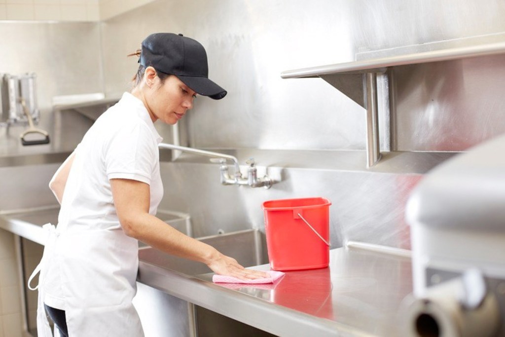 woman in restaurant kitchen wiping down food prep area