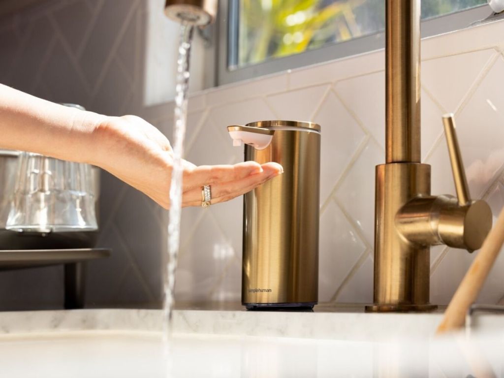 woman's hand using touch free soap dispenser at sink with water running