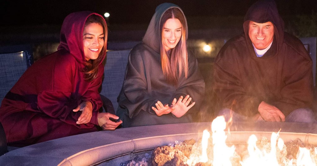 people wearing oversized hoodies around a fire