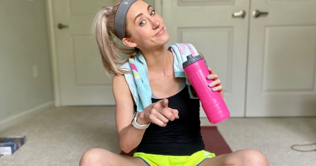 Woman sitting on the floor in workout clothes holding a water bottle