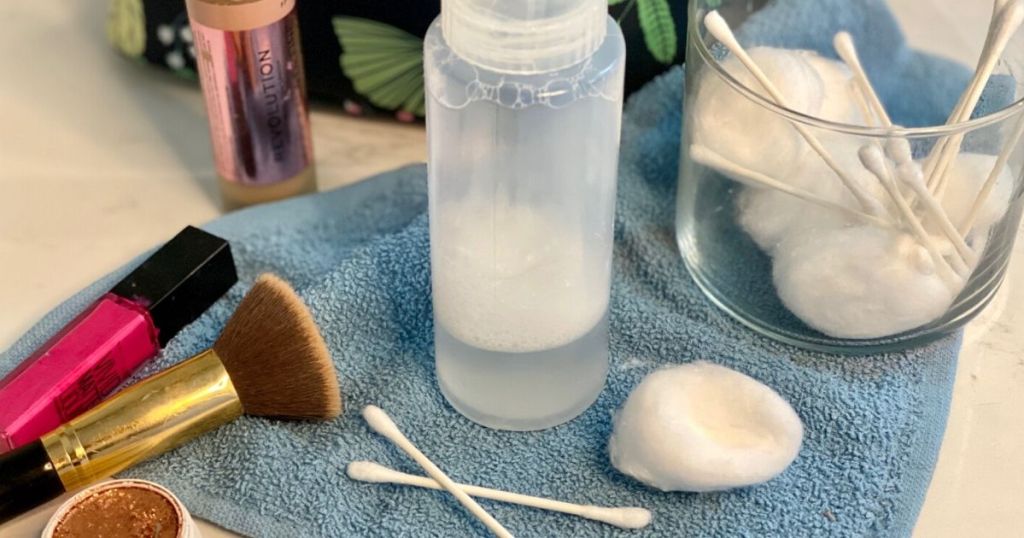 DIY makeup remover, Q-tips, and cotton balls on a bathroom counter next to makeup items