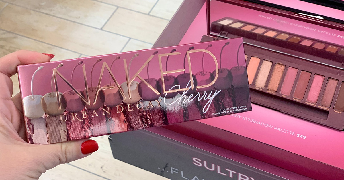 woman holding up the urban decay cherry eyeshadow palette box in front of the opened eyeshadow palette in background