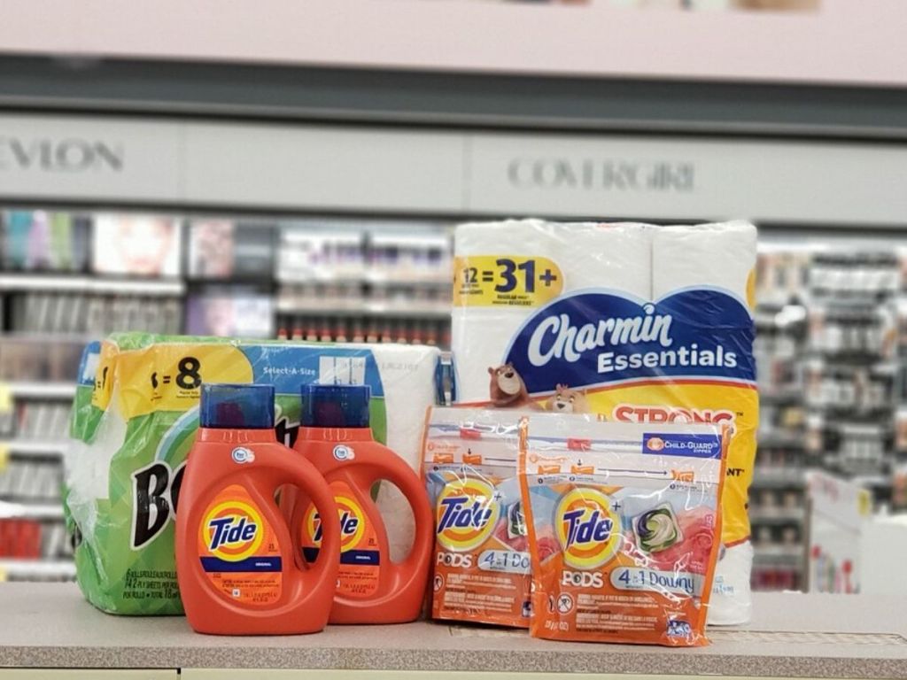 counter at store with paper towels, two bottles of laundry detergent, a pack of toilet paper, and two packages of laundry pods