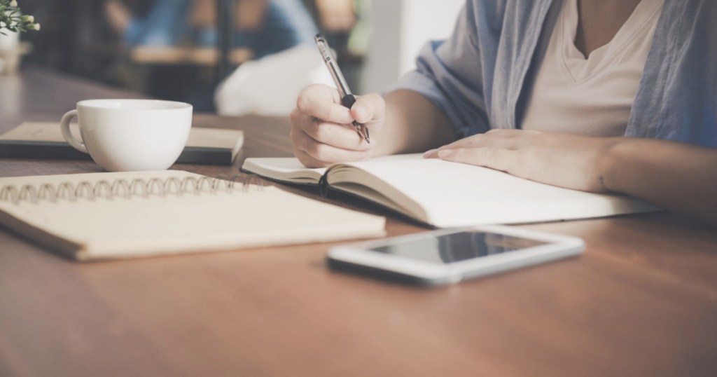 Woman writing in notebook with tablet next to her