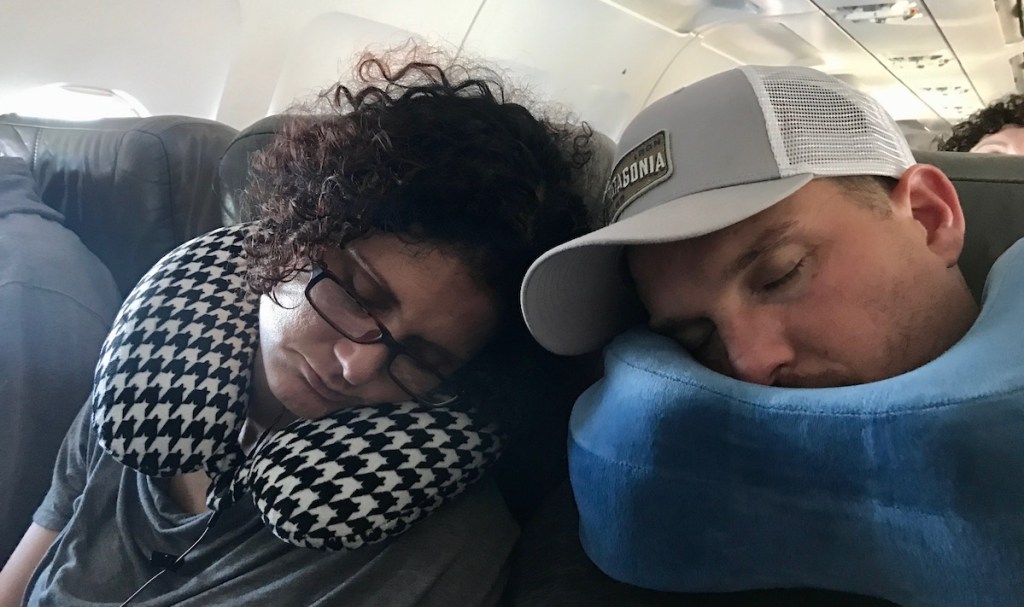 woman and man sleeping with neck pillows on airplane