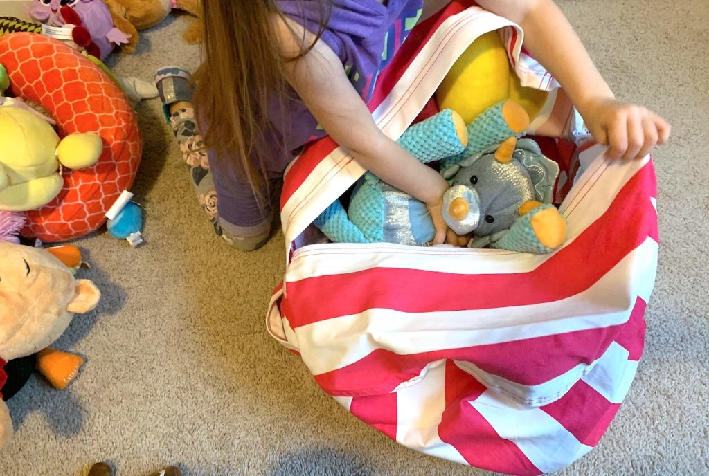 girl putting stuffed animals into hot pink and white stripe bean bag chair