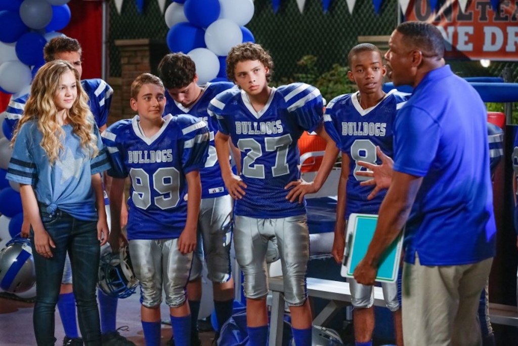 girl standing with boys wearing football uniforms talking to coach