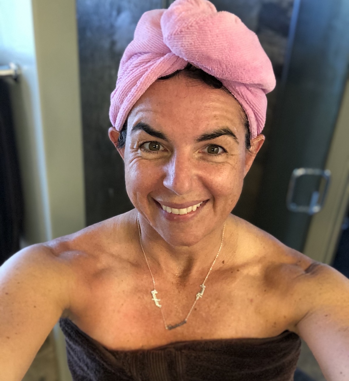 woman wearing pink towel on head with name necklace on 