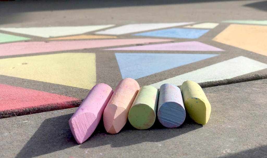various colors of sidewalk chalk laying in front of stained glass painted art on sidewalk