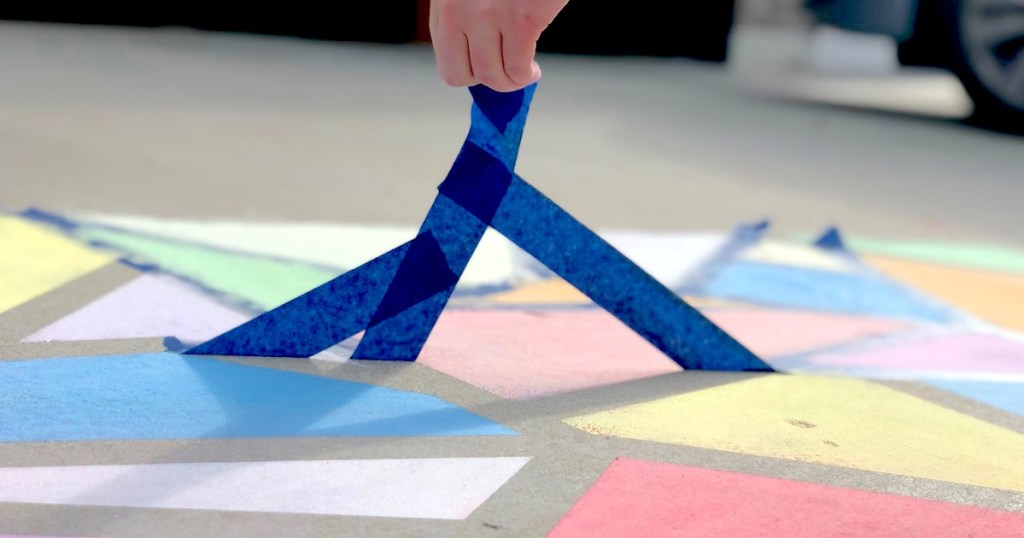 hand pulling blue painters tape off concrete with chalk stained glass art