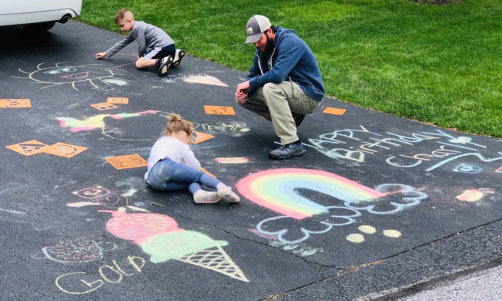 man and kids writing with chalk on driveway 
