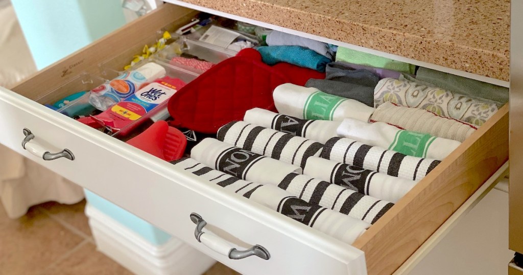wide drawer with folded white and black towels with other various kitchen items
