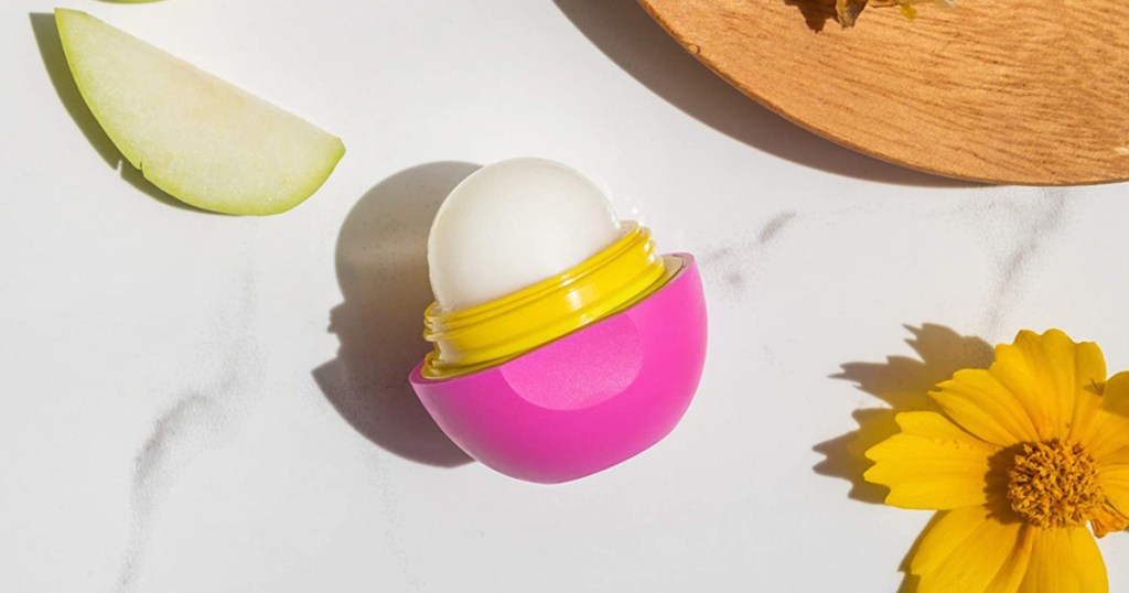 pink sphere of lip balm on counter with yellow slower and apple slice