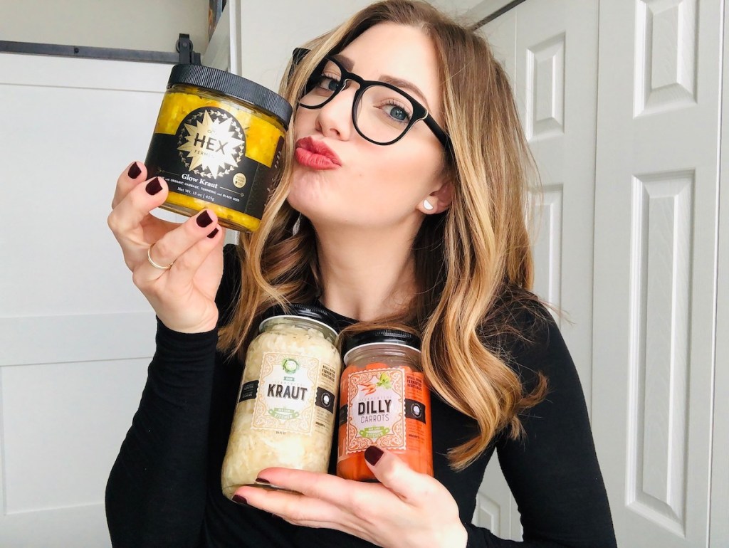 woman kissing jar of yellow kraut holding other jars of fermented food