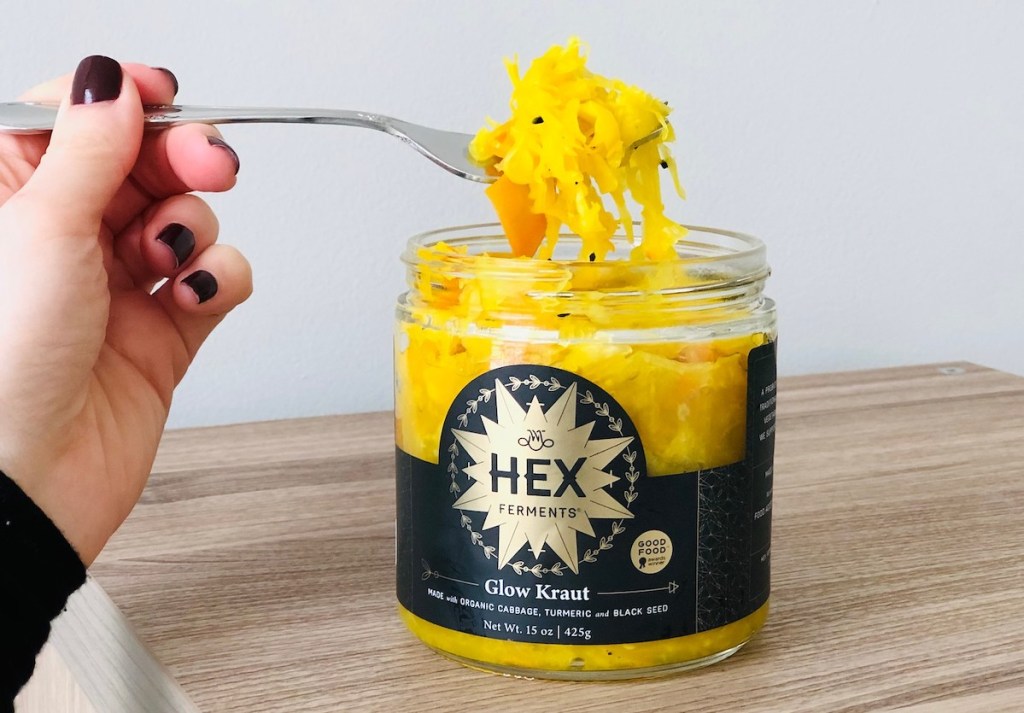hand holding fork with bright yellow kraut on it over jar
