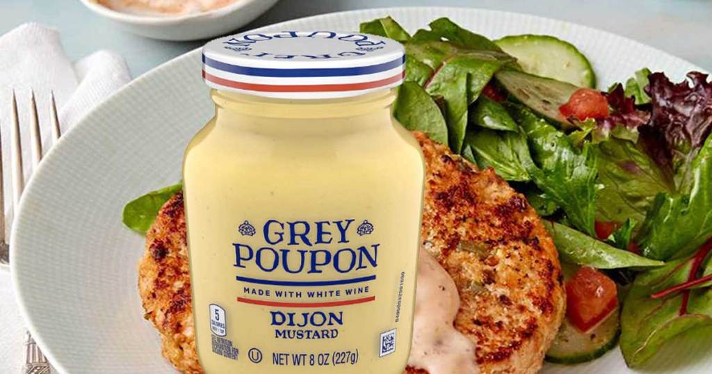grey poupon Dijon mustard sitting in front of a plate of food