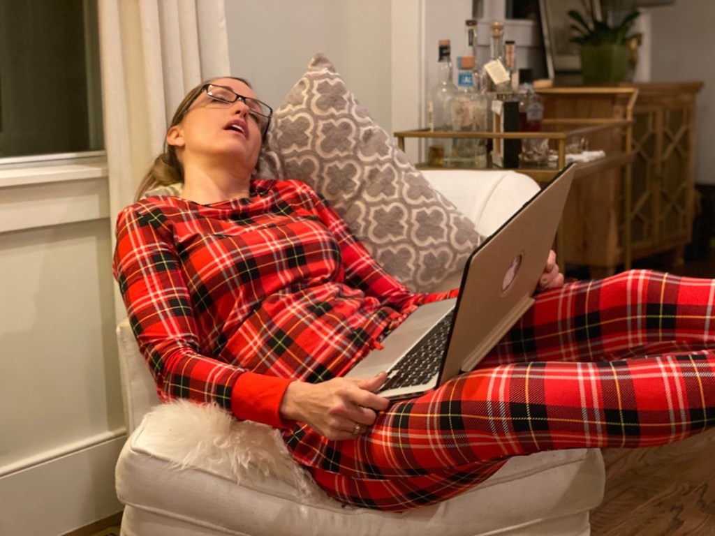 woman wearing red plaid pajamas sleeping on chair with laptop on lap