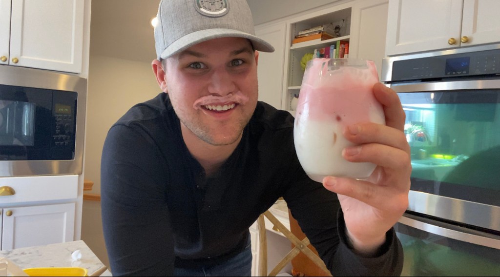 man smiling with pink milk mustache holding a drinking glass with pink beverage