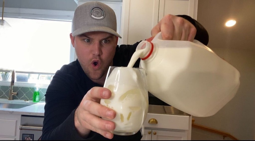 man holding a gallon of milk and glass with ice and milk inside