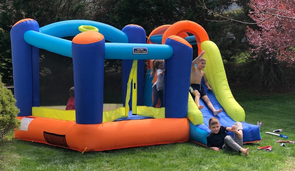 kids jumping on colorful moon bounce outside in yard