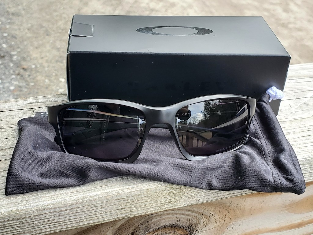 oakley black men's glasses sitting on pouch and in front of box 