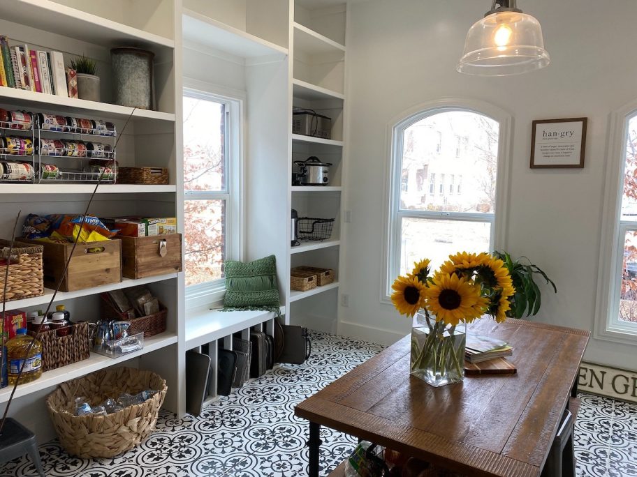 Beautiful organized white pantry room with baskets and table in middle of floor with flowers