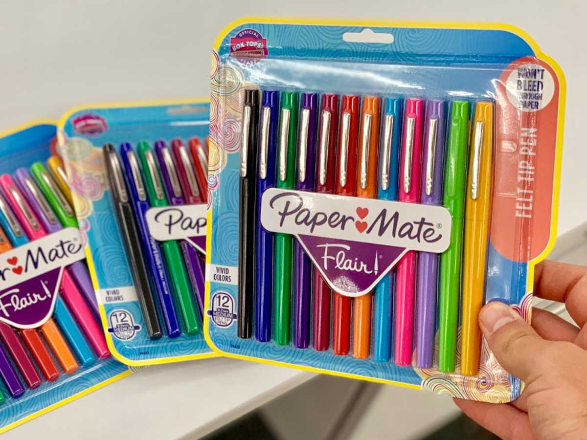 hand holding a paper mate package of markers with 2 packs on a table behind him