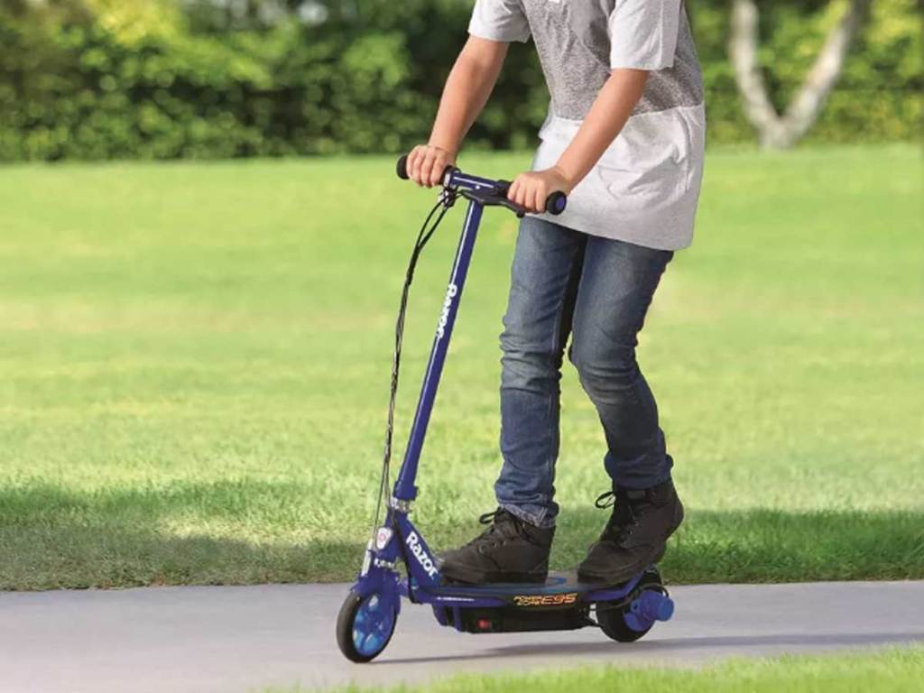 boy riding a blue electric scooter through a park