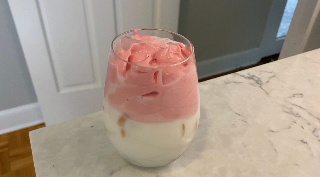 glass sitting on countertop with half milk and pink fluffy strawberry whipped cream