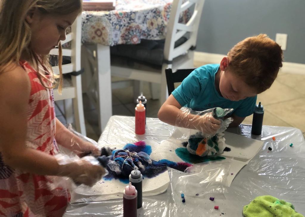 two kids at table tie dying shirts with various colors