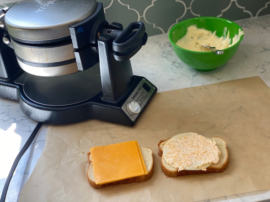waffle maker with grilled cheese sandwich ingredients on parchment paper 