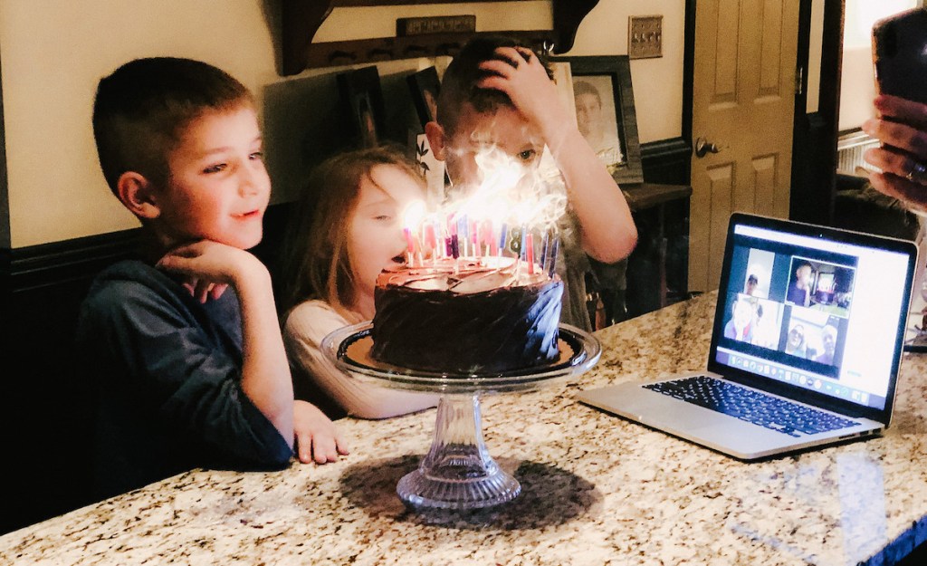 kids standing in front of cake with candles with computer on granite countertop