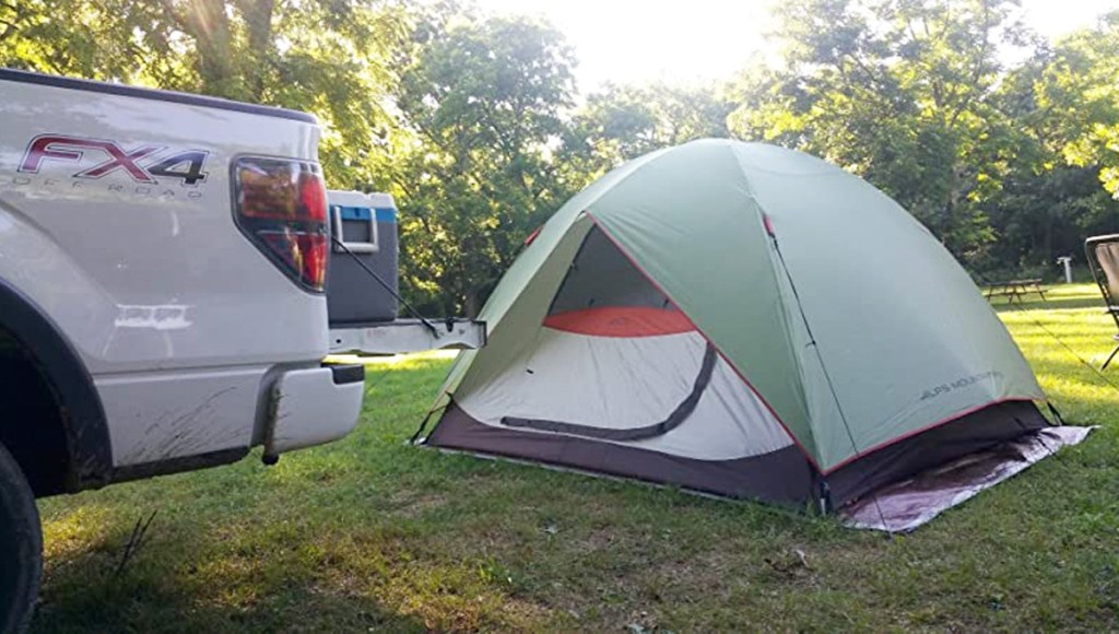 light grey tent with green rain shield set up next to white truck with cooler