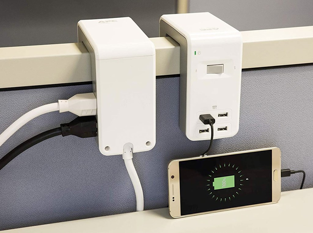 two white u-shaped surge protectors hanging over cubical wall with phone plugged in and charging
