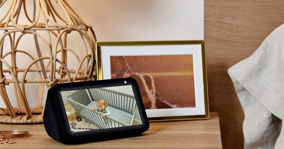 Amazon Echo Show sitting on a nightstand next to a lamp and picture frame