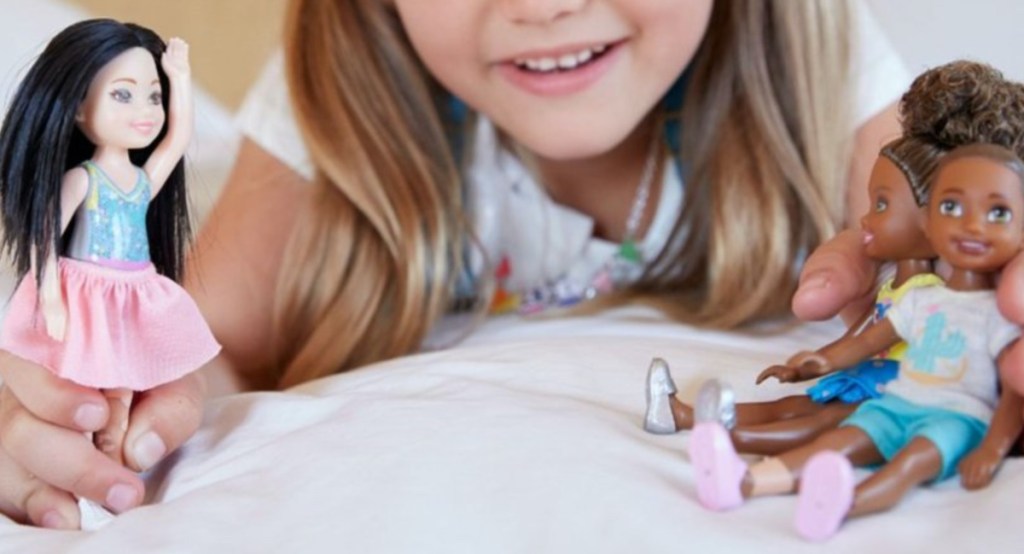girl playing with three dolls on bed
