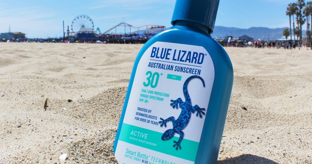 blue bottle of sunscreen in sand on beach with boardwalk in background