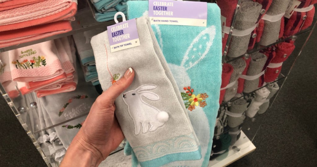 manicured hand holding gray, blue-trimmed bunny hand towel and blue bunny hand towel in front of hand towels display in store