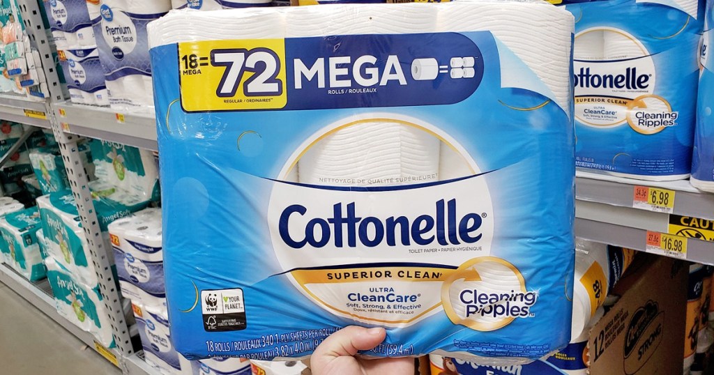 person holding up a blue package of cottonelle toilet paper in paper good aisle of store