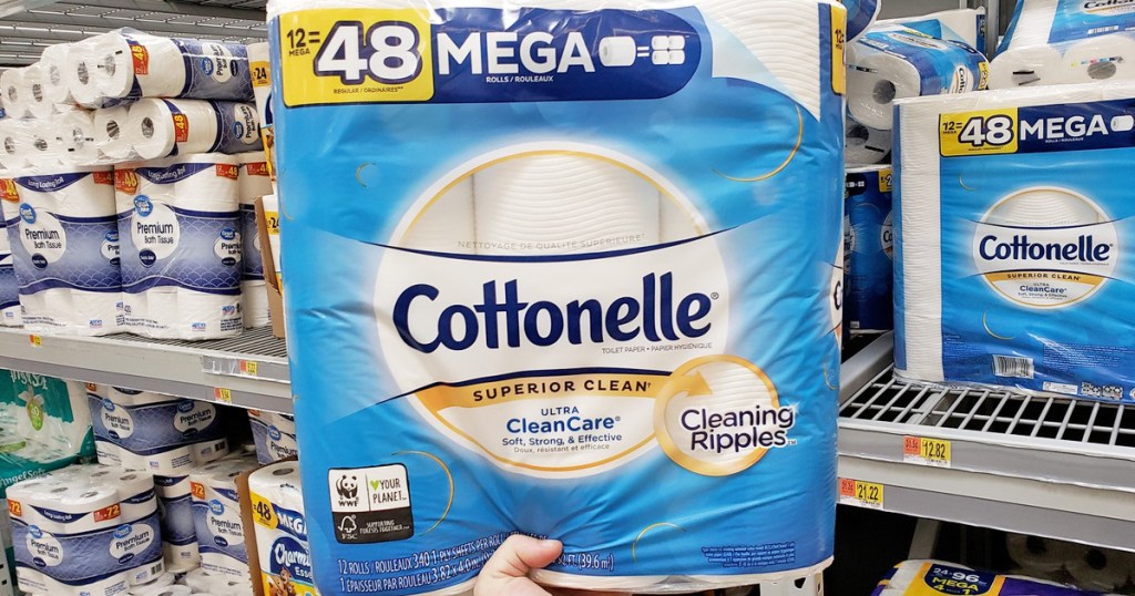 person holding a blue package of Cottonelle toilet paper in front of store display waste of money