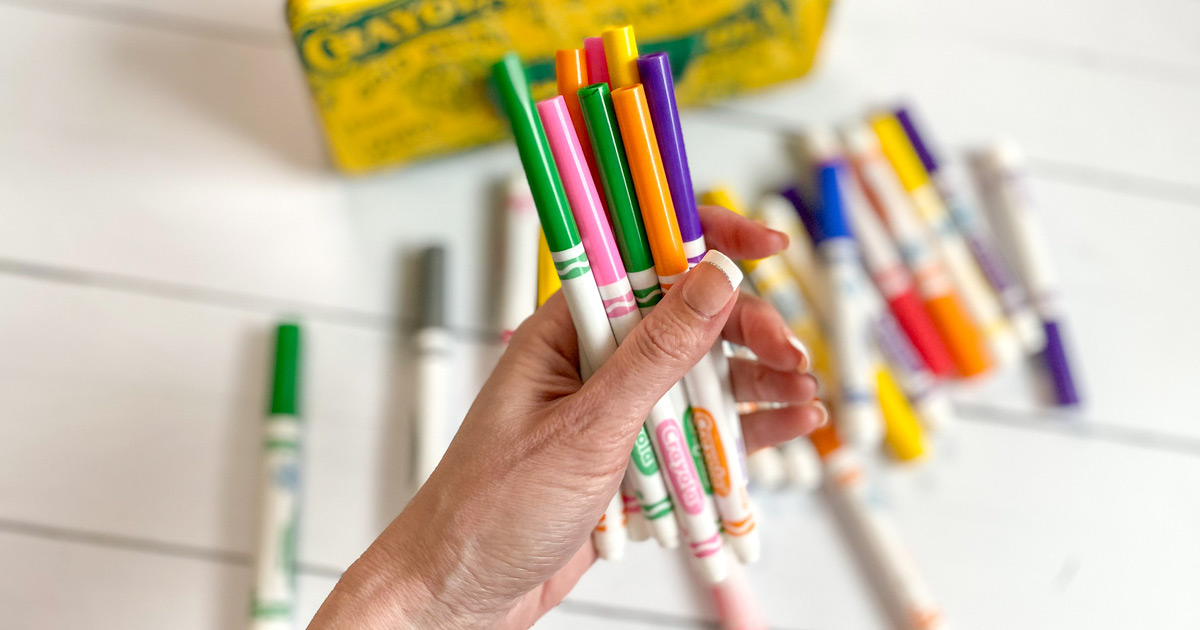 person holding a handful of colorful crayola markers with other markers in background