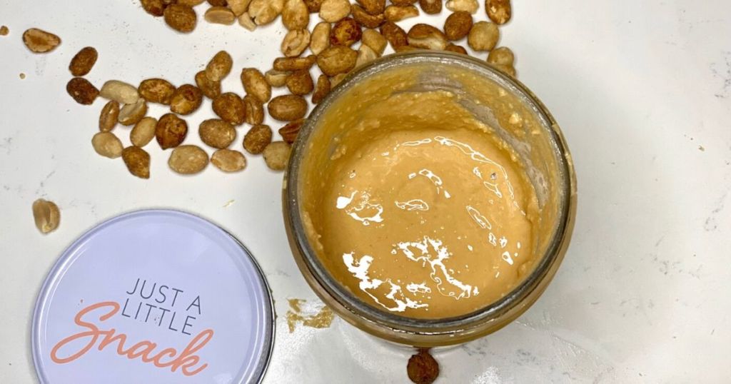 Homemade peanut butter in a jar next to peanuts on the counter
